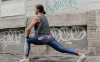 Woman doing lunges for fitness against an urban graffiti wall, showcasing exercise and wellness.