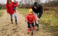 Happy family walking outdoors in fall, teaching child to ride bike.